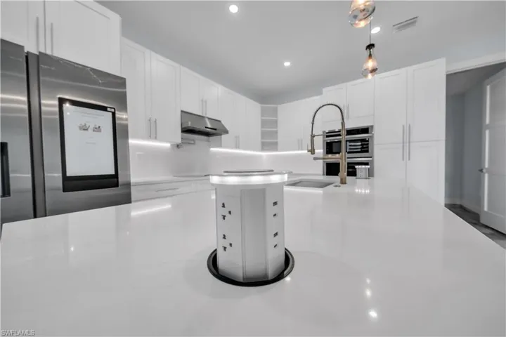 Kitchen featuring white cabinetry, stainless steel appliances, light stone countertops, and hanging light fixtures