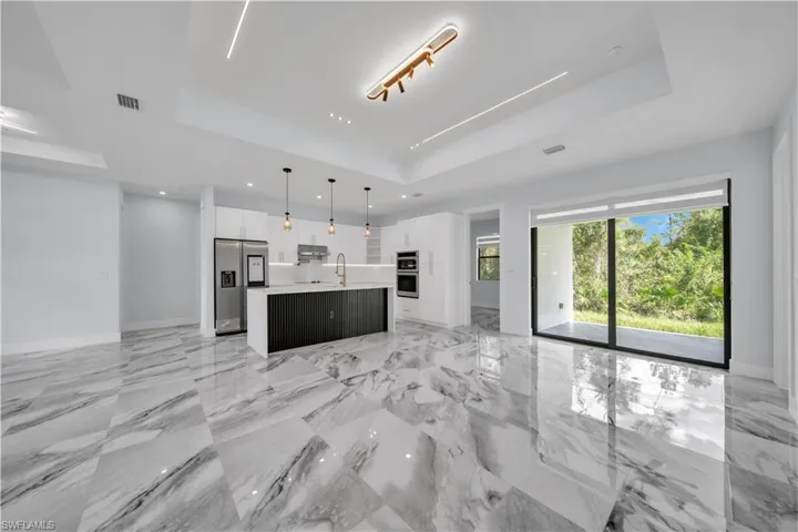 Two tone kitchen with pendant lighting, stainless steel appliances, open floor plan, a raised ceiling, and a center island