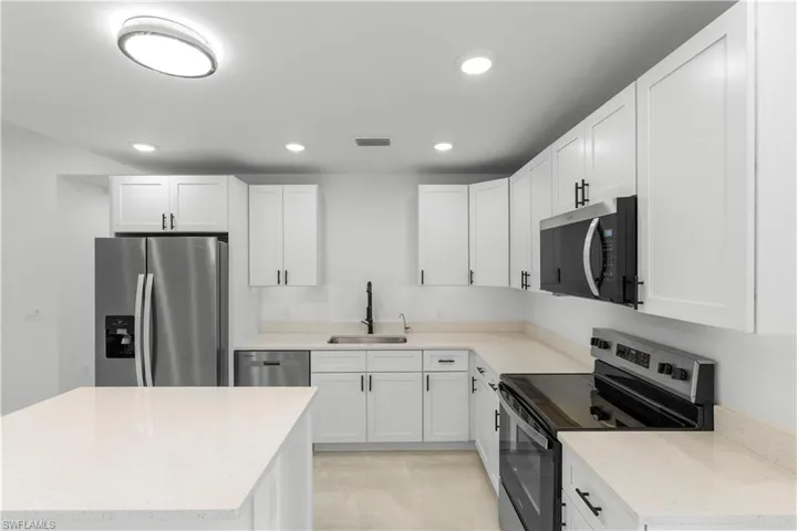 Kitchen featuring appliances with stainless steel finishes, white cabinetry, light stone counters, and recessed lighting