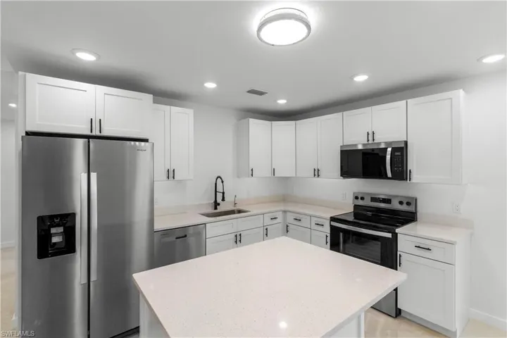 Kitchen with appliances with stainless steel finishes, white cabinets, recessed lighting, light stone countertops, and a center island