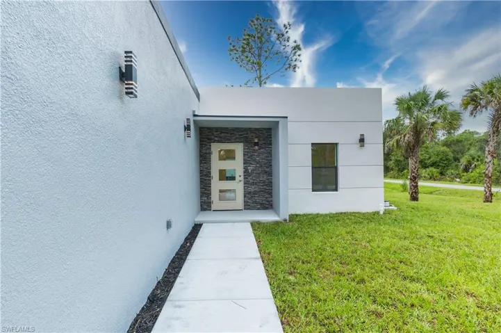 Entrance to property featuring a lawn, stone siding, and stucco siding