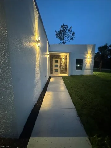 Exterior entry at night with a yard and stucco siding