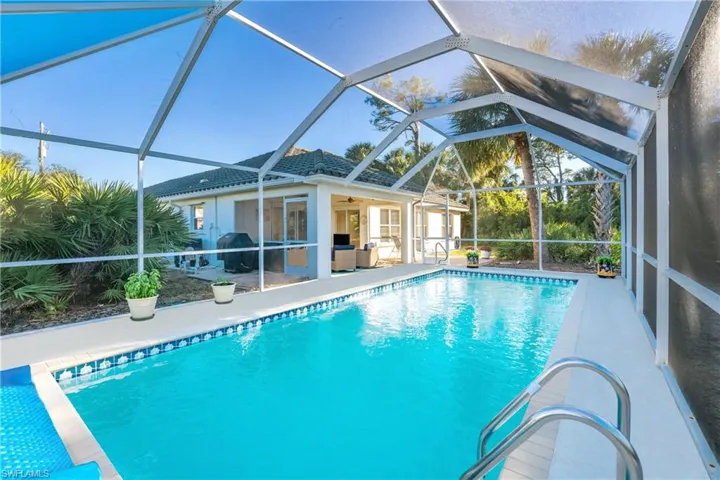 View of pool with glass enclosure, ceiling fan, and a patio area
