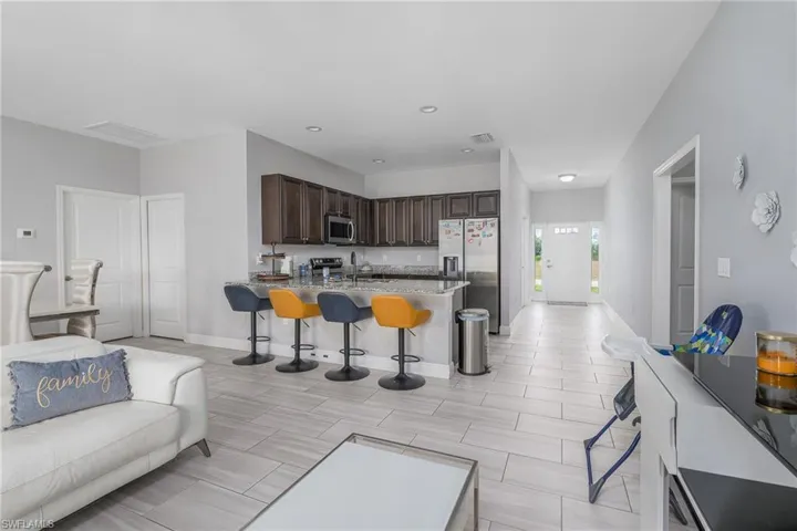 Open-concept living area featuring light wood-finish tile flooring, recessed lighting, and a white paneled front door with side lites