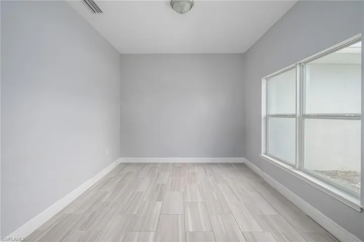 Spacious room featuring light gray wall paint, white baseboards, and wood-finish tile flooring