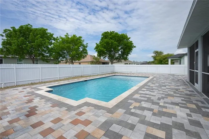 Outdoor swimming pool with integrated spa, surrounded by multi-toned paver decking and a white privacy fence