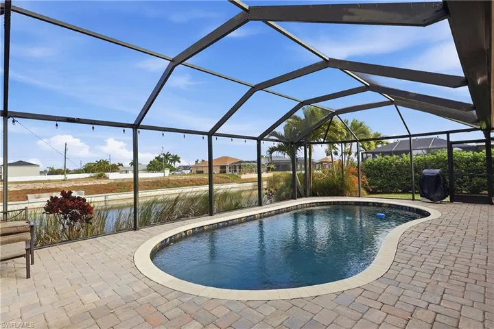 Outdoor pool with glass enclosure, a sunroom, a grill, and a patio area