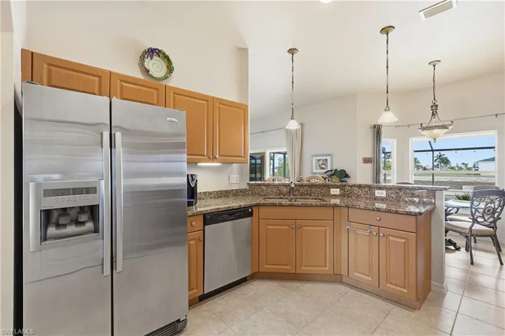 Kitchen with appliances with stainless steel finishes, dark stone counters, a peninsula, decorative light fixtures, and brown cabinets