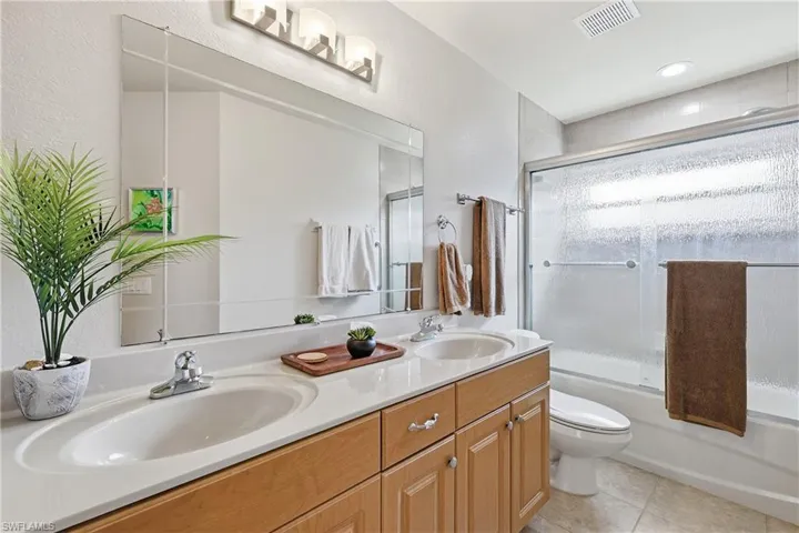 Bathroom featuring double vanity, bath / shower combo with glass door, and light tile patterned flooring