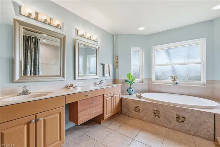 Bathroom with a garden tub, a shower with shower curtain, double vanity, and light tile patterned flooring