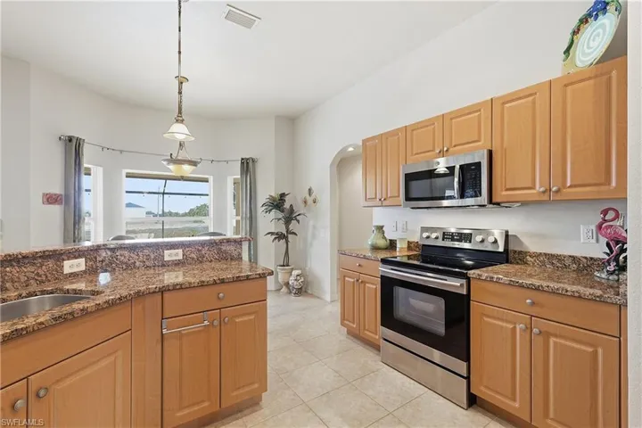 Kitchen with stainless steel appliances, arched walkways, dark stone countertops, pendant lighting, and light tile patterned flooring
