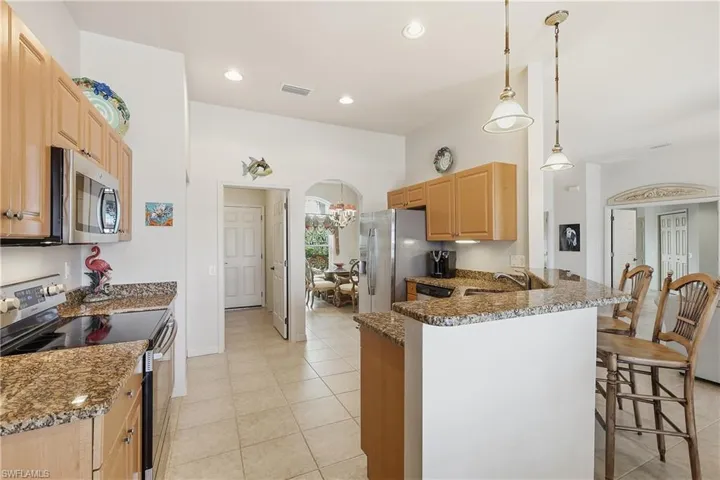 Kitchen with appliances with stainless steel finishes, hanging light fixtures, dark stone counters, a peninsula, and light brown cabinetry