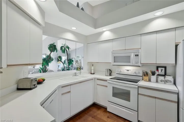 Kitchen with white appliances, light countertops, dark wood-style floors, white cabinets, and recessed lighting