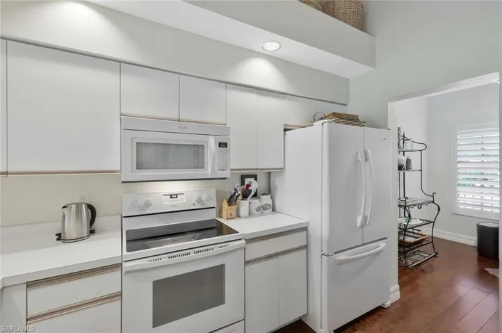 Kitchen featuring white appliances, light countertops, dark wood-type flooring, and white cabinets