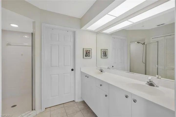 Bathroom featuring a shower stall, double vanity, light tile patterned flooring, and a closet
