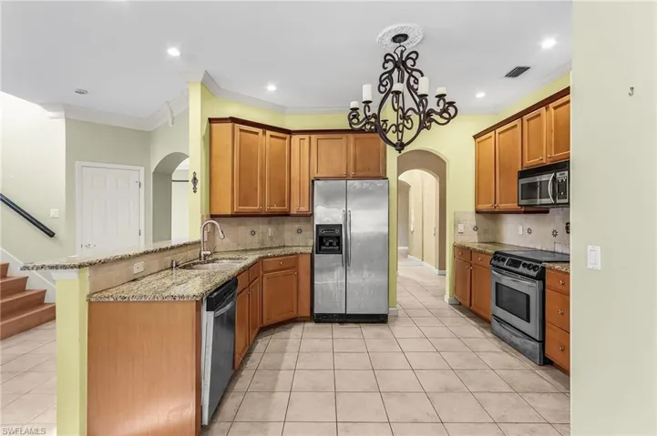 Kitchen featuring arched walkways, stainless steel appliances, a peninsula, light stone counters, and light tile patterned floors