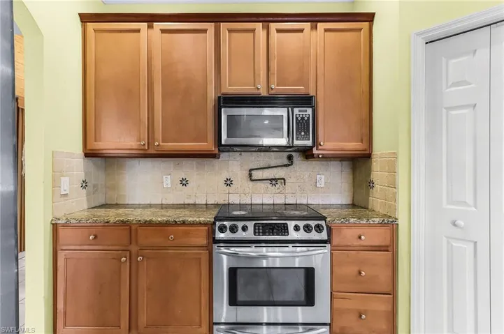 Kitchen featuring stainless steel electric stove, dark stone counters, wood finish cabinets, and backsplash