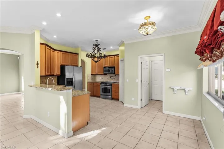 Kitchen featuring arched walkways, wood finish cabinetry, light tile patterned floors, stainless steel appliances, and ornamental molding