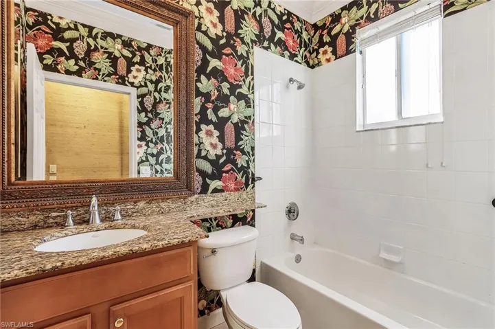 Full bathroom with wallpapered walls, vanity, and shower / tub combination