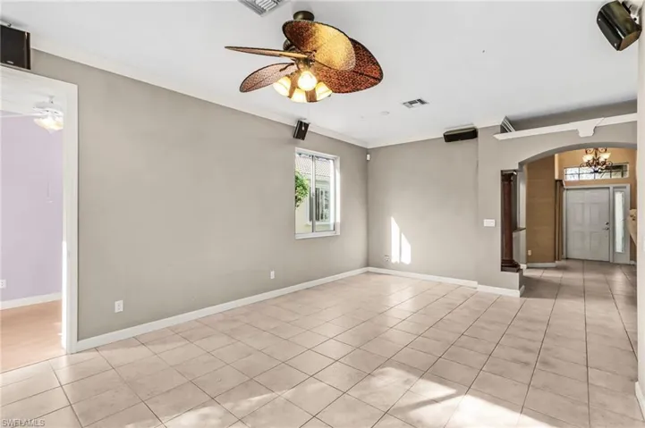 Empty room with arched walkways, crown molding, a ceiling fan, and light tile patterned flooring