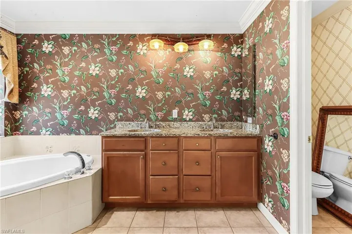 Bathroom featuring wallpapered walls, double vanity, light tile patterned floors, a garden tub, and ornamental molding