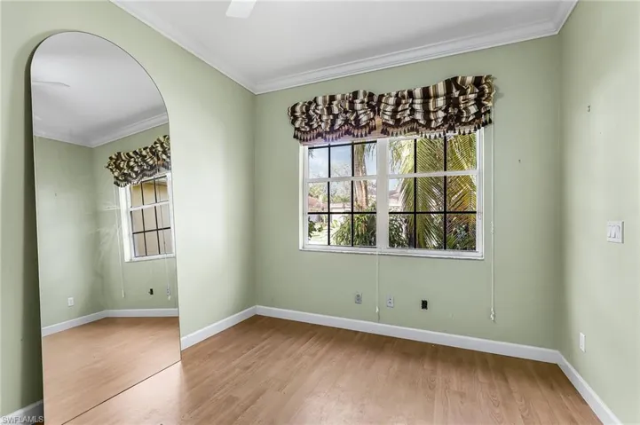 Spare room with arched walkways, crown molding, light wood-style floors, and plenty of natural light
