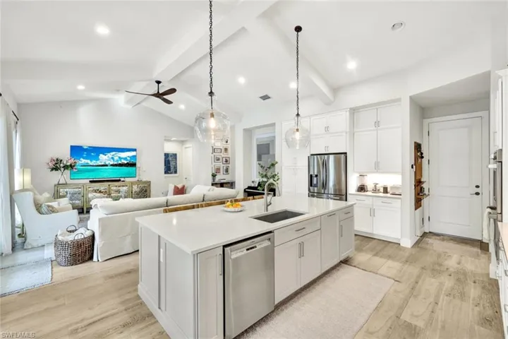Kitchen with white cabinetry, stainless steel appliances, hanging light fixtures, a kitchen island with sink, and open floor plan