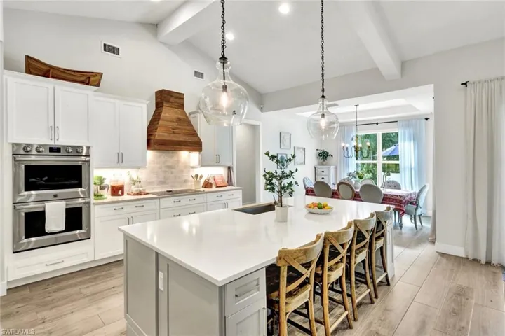 Kitchen featuring white cabinetry, double oven, custom range hood, decorative light fixtures, and light wood-type flooring