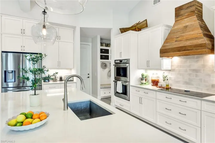 Kitchen featuring white cabinetry, stainless steel appliances, custom range hood, decorative light fixtures, and light stone counters
