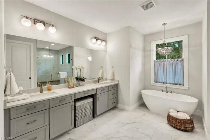 Bathroom featuring double vanity, a marble finish shower, a soaking tub, and light marble finish floors