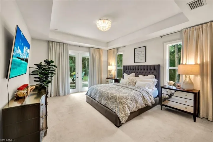 Bedroom with french doors, a raised ceiling, access to outside, light carpet, and multiple windows