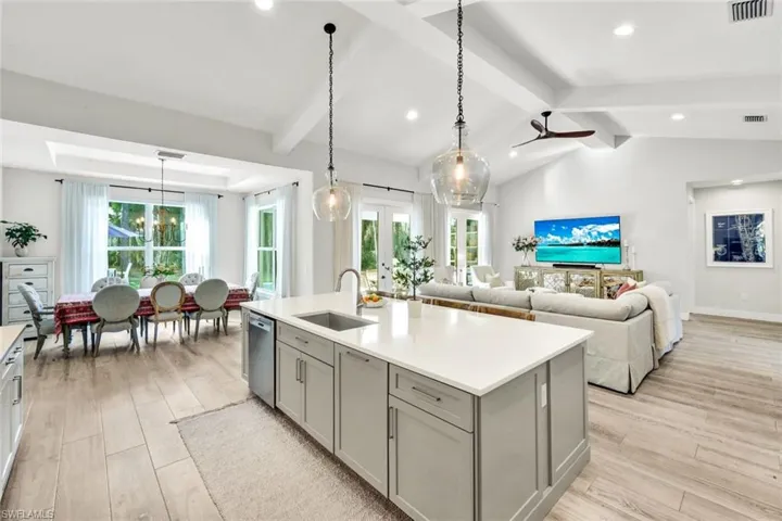 Kitchen featuring gray cabinets, decorative light fixtures, light wood-style floors, a center island with sink, and open floor plan