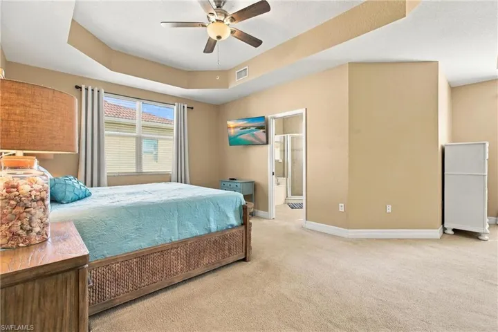Tray ceiling, carpeted flooring, and a ceiling-mounted light fixture with fan