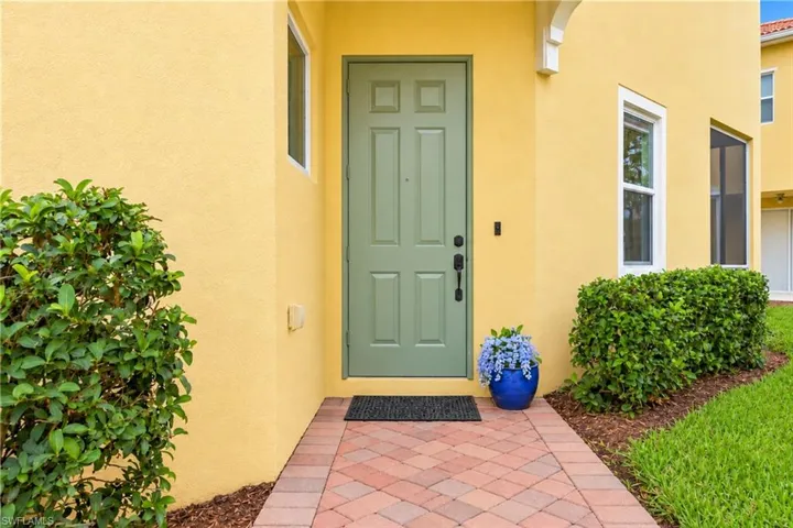Stucco exterior featuring a six-panel entry door in a muted green finish, complemented by a brick-paver walkway and structured landscaping