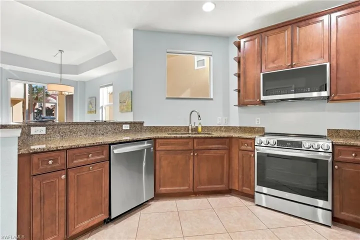 Kitchen featuring wood cabinetry, stone countertops, stainless steel appliances, and ceramic tile flooring