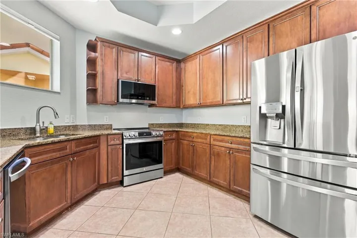 Kitchen featuring wood cabinetry, stone countertops, stainless steel appliances, ceramic tile flooring, and a tray ceiling