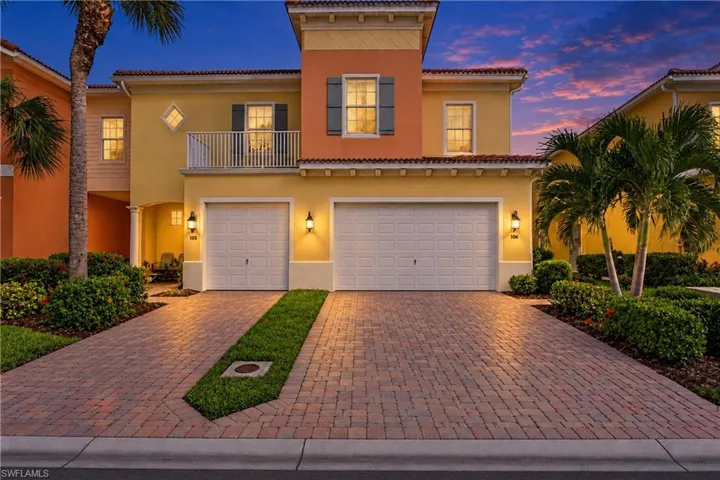 Stucco exterior featuring a paver driveway, three-bay garage configuration, second-story balcony with metal railing, and decorative shutters