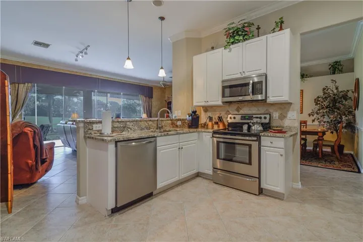 Kitchen featuring white raised panel cabinetry, tasteful backsplash, eclectic brown and gold granite, stainless steel appliances, and breakfast bar