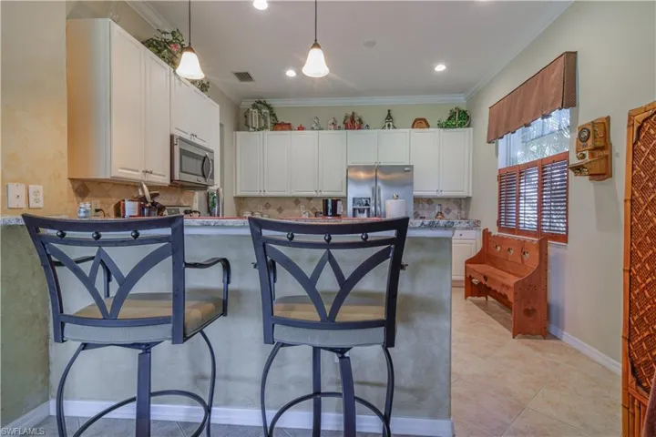 Kitchen featuring white raised panel cabinetry, tasteful backsplash, eclectic brown and gold granite, stainless steel appliances, and breakfast bar