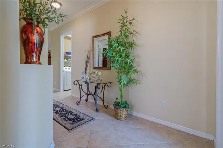 Corridor with washer / clothes dryer, crown molding, and light tile patterned floors