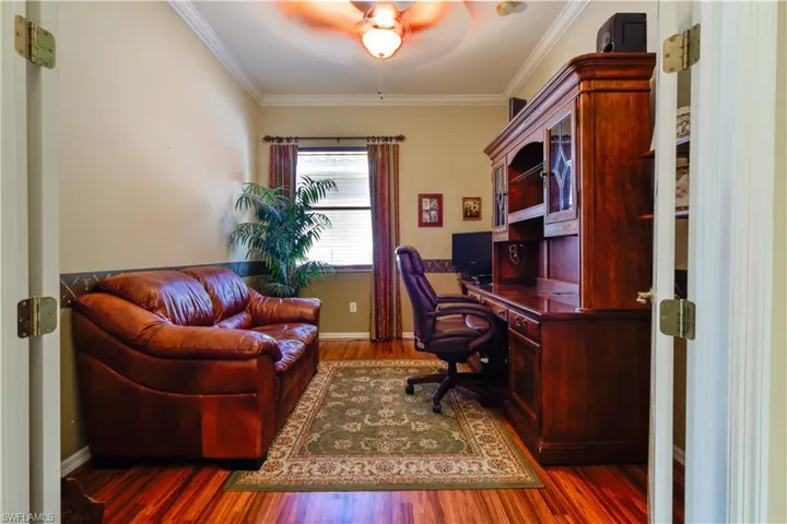 Den featuring medium Cherry Finish laminate wood-style flooring, crown molding, and ceiling fan