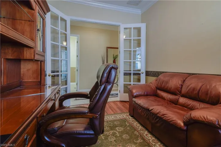 Den featuring medium Cherry Finish laminate wood-style flooring, crown molding, and ceiling fan