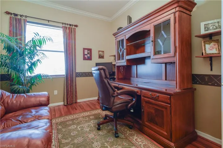 Den featuring medium Cherry Finish laminate wood-style flooring, crown molding, and ceiling fan