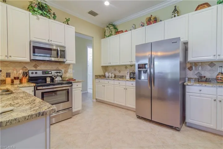 Kitchen featuring white raised panel cabinetry, tasteful backsplash, eclectic brown and gold granite, and stainless steel appliances
