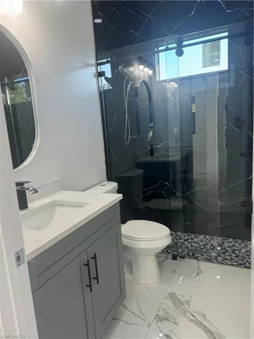 Bathroom featuring an enclosed shower, tile flooring, vanity, and toilet