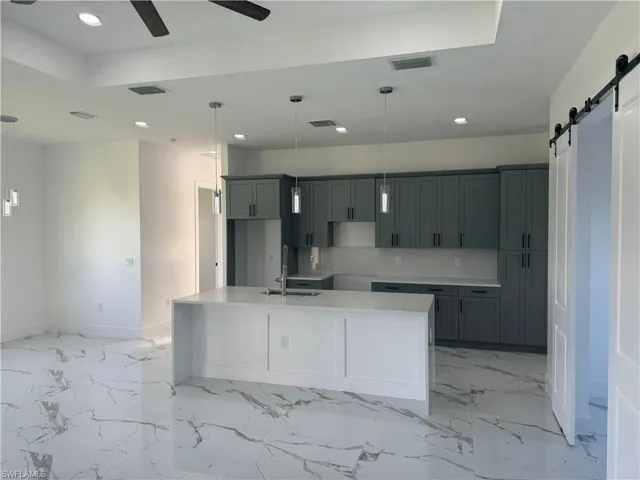 Kitchen with ceiling fan, an island with sink, a barn door, sink, and light tile floors