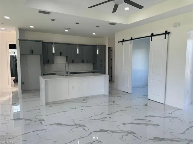 Kitchen with decorative light fixtures, ceiling fan, an island with sink, a barn door, and sink