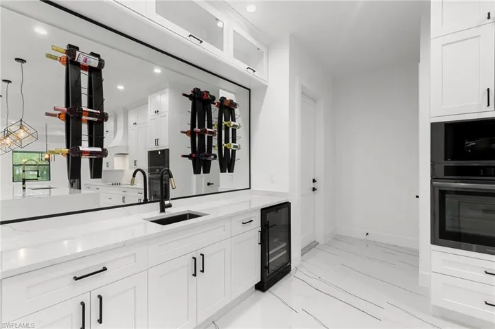 Kitchen with beverage cooler, light stone counters, white cabinetry, and sink