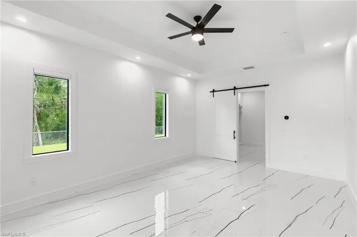 Unfurnished room featuring ceiling fan, a raised ceiling, and a barn door