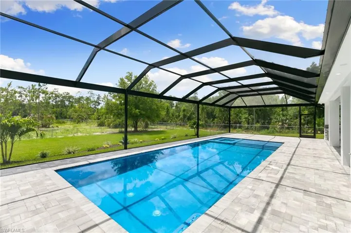 View of pool featuring a lawn, a patio, and glass enclosure